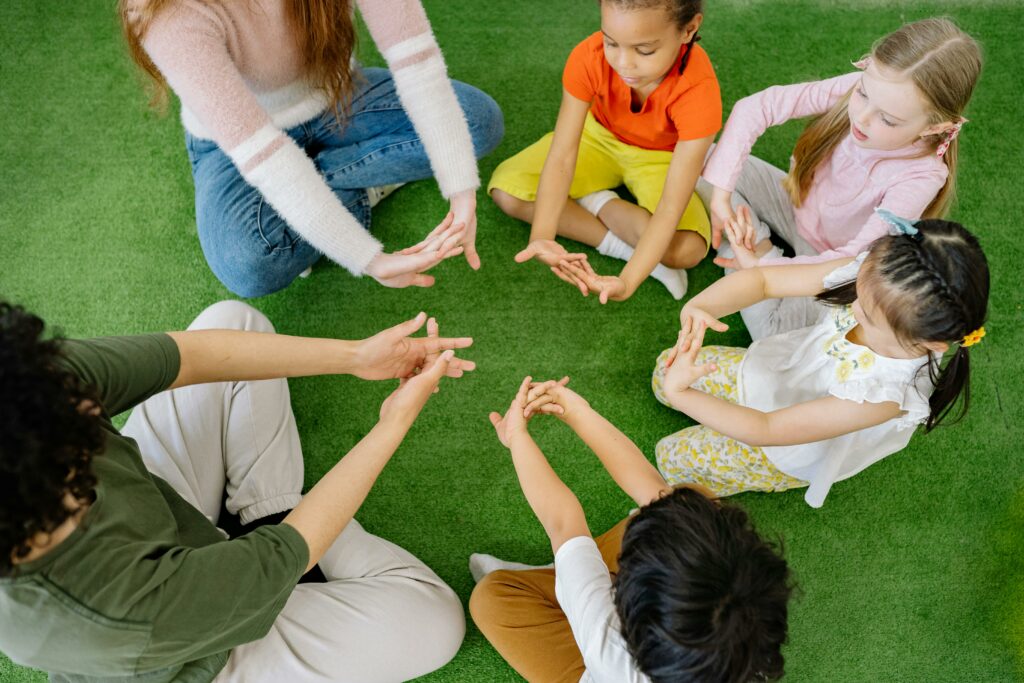Children with teacher sitting in circle on the floor stretching arms